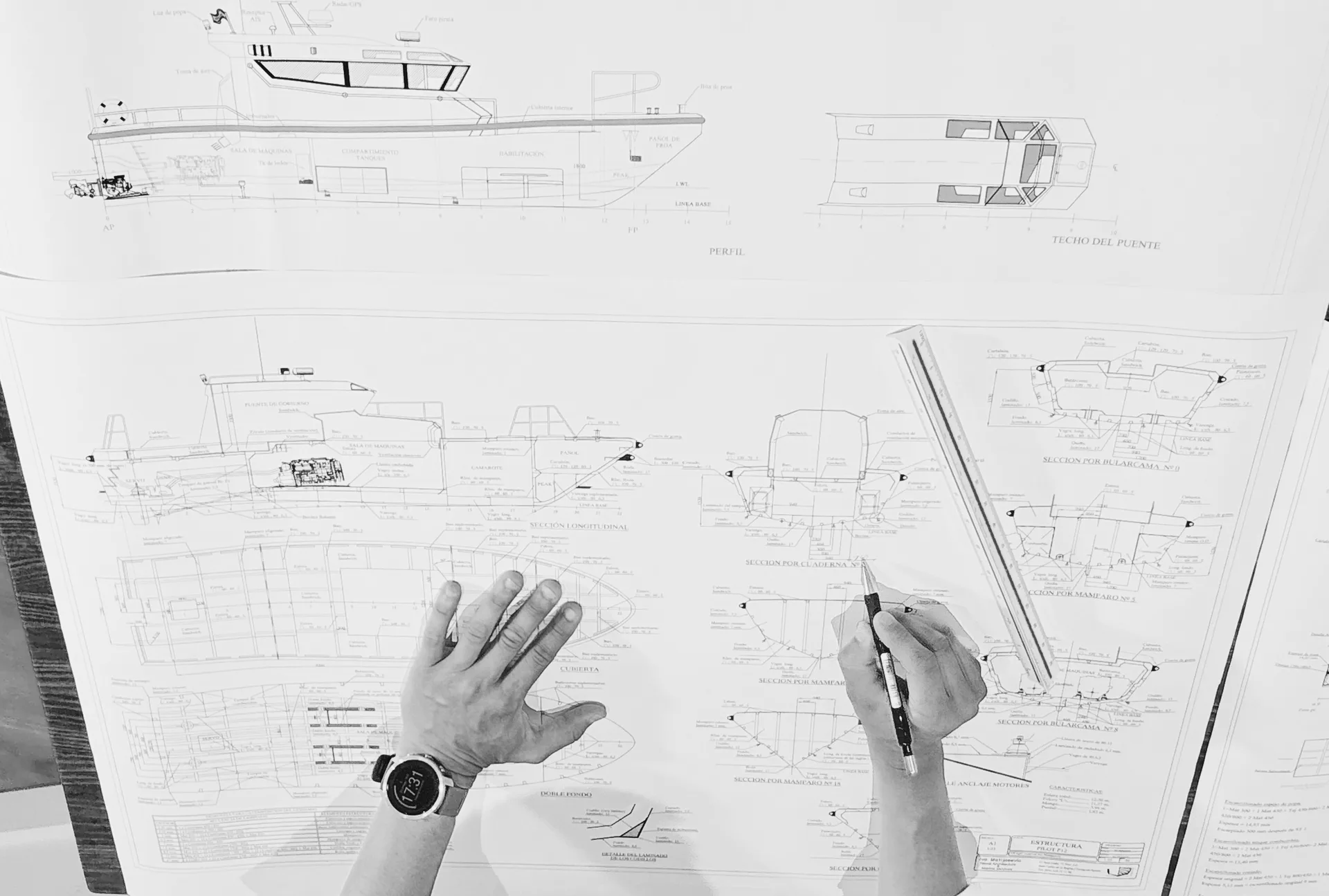 Planos técnicos de arquitectura naval extendidos sobre una mesa de trabajo, con detalles de secciones del casco.