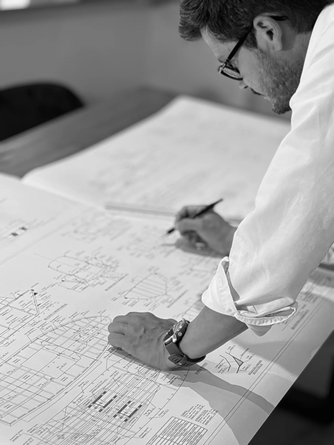 Ingeniero naval de OCEANAVAL trazando a mano sobre los planos técnicos de una embarcación en la oficina técnica, en blanco y negro.
