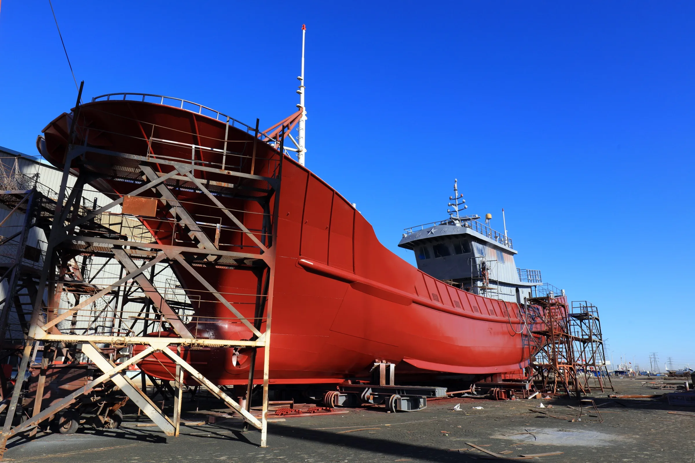 Casco de embarcación profesional de color rojo en dique seco con andamiaje, durante un proyecto de reforma de OCEANAVAL.