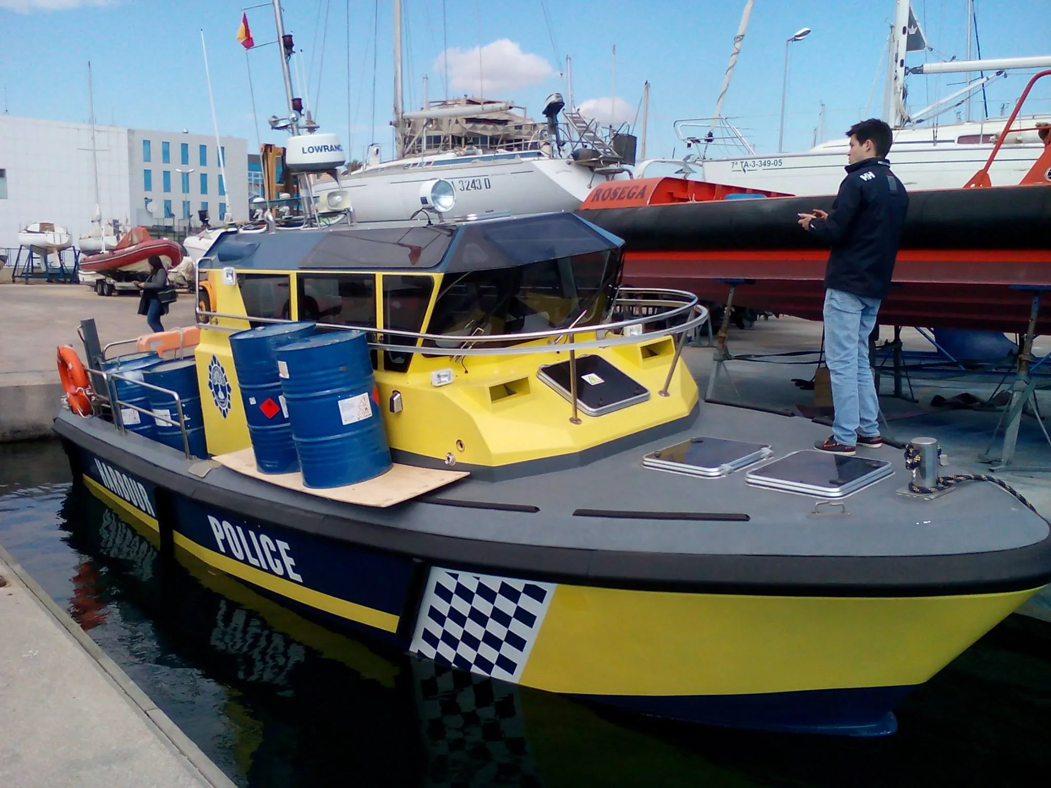 Ingeniero de OCEANAVAL sobre la cubierta de una embarcación de policía portuaria amarilla y azul en dique seco, durante una inspección a pie de casco.
